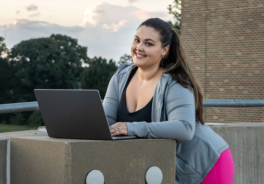 A photo of the coach outdoors working with their laptop.